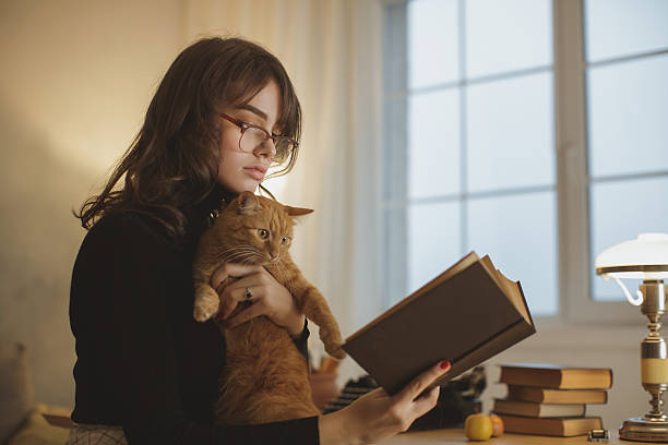 istock Young Woman Reading Book With Cat In Cozy Study Room 2217422055