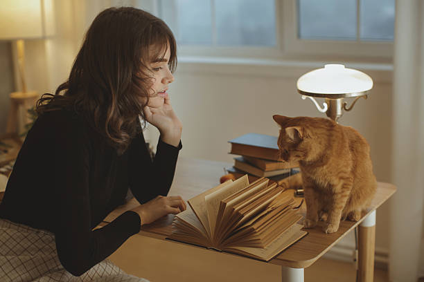 istock Young Woman Reading With Cat On Desk In Cozy Study Room 2217422194