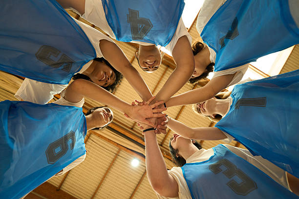 Group of teenage girls wearing white t-shirts and black shorts practicing basketball throws, standing in a row in gym. Wide angle view.