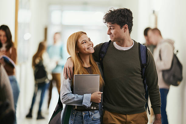 istock Happy college couple talking while walking embraced in a hallway. 2217423401
