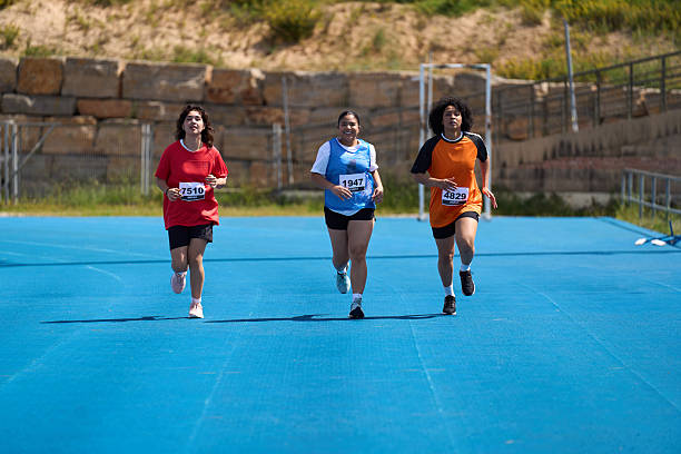 Three determined female athletes are running a race on a vibrant blue track, striving for victory