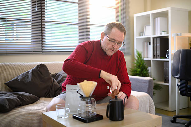 istock Senior man in a red sweater making pour over coffee with a glass dripper and kettle 2217427016