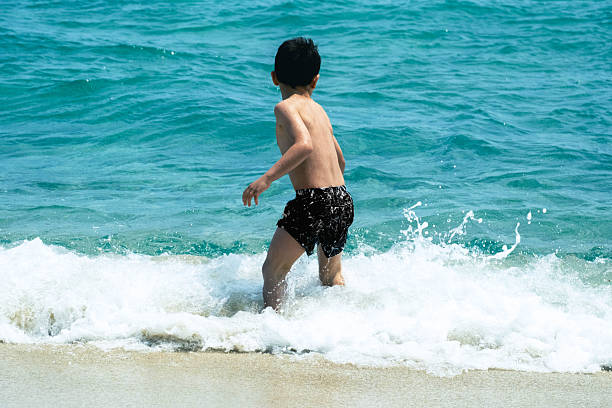 A child plays in the waves at the seaside. The sea is a bit rough and the child seems to be afraid of the waves. The day is sunny and it is perfect for being at the seaside and playing