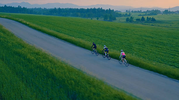 istock Three cyclists ride on a country road, surrounded by green fields and hills 2217427614