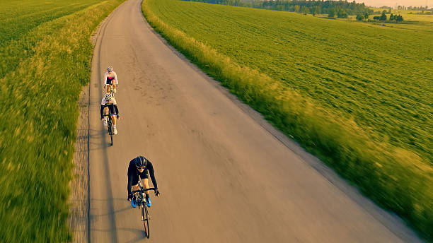 Vital caucasian couple moving fast downhill during their bike ride in the mountains. They are fast and aerodynamic. The background is blurred due to the high speed of the cyclists. The weather is nice and the sun is shining. Active weekend for recreational cyclists.