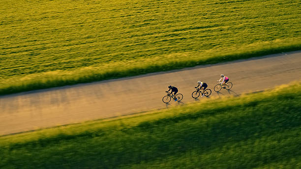 istock Three cyclists race on a country road, surrounded by lush green fields 2217427652