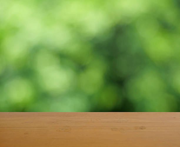 istock Empty brown wooden table surface for product placement with bokeh from green leaves in background 2217428174