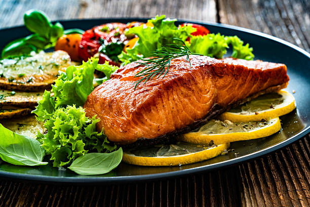 istock Fried salmon steak with fried potatoes, lemon and fresh vegetables served on black plate on wooden background 2217432833