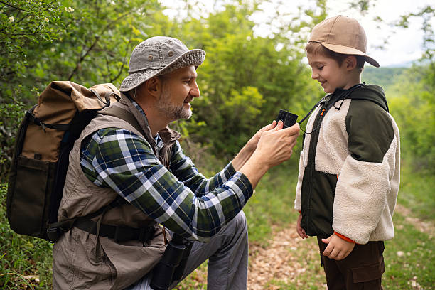 Father and son explore the outdoors, bonding while birdwatching amidst a picturesque forest trail. The enthusiasm for nature and wildlife strengthens their bond.