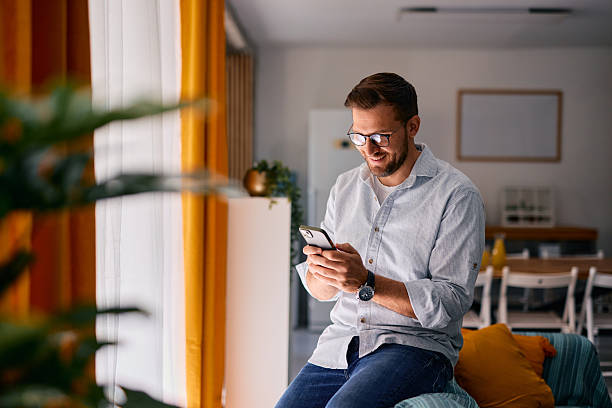 istock Young man using mobile phone and smiling while sitting at home 2217440347