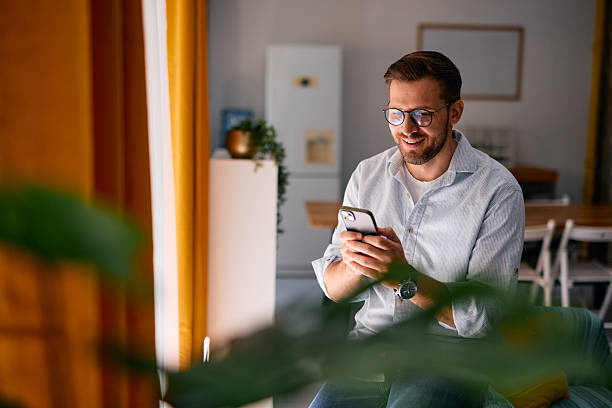 istock Smiling man using smartphone at home, sending messages and browsing internet 2217440348