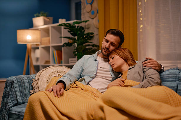 istock Exhausted couple sleeping on sofa under warm blanket in living room 2217440600