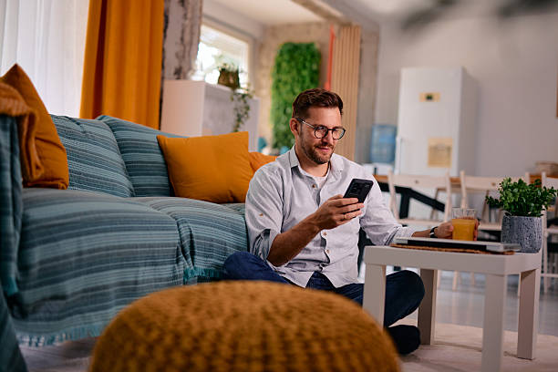 istock Man relaxing on living room floor using smartphone and drinking juice 2217441203