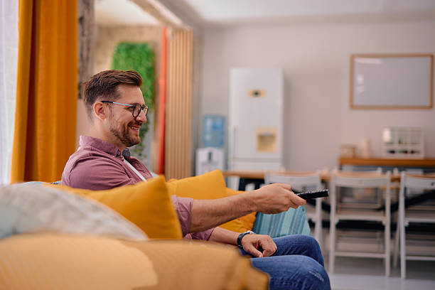 istock Man relaxing on sofa watching television changing channels with remote control 2217441407