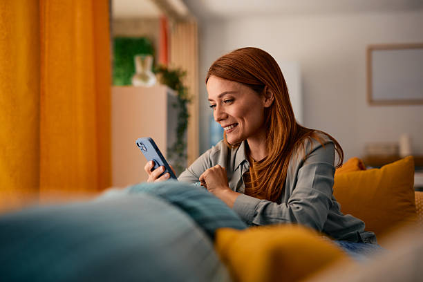 Happy woman relaxing on sofa using mobile phone at home