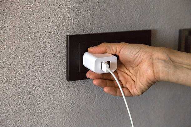 A person is plugging a white USB charger into a black wall socket, symbolizing daily use of modern technology for powering electronic devices indoors.