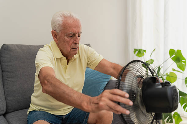 istock Senior man refreshing with electric fan at home while sitting on sofa during hot day in summer 2217450199
