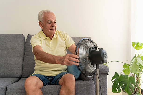 istock Senior man refreshing with ventilator while sitting on sofa at home during hot weather 2217450212