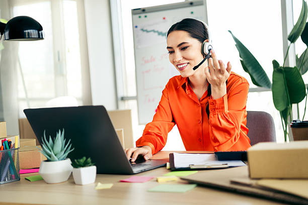 istock Young female entrepreneur with headset working on laptop in an office setting managing ecommerce retail business 2217452275