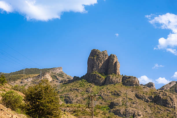 Majestic twin rock formations rise prominently from a rugged mountain landscape. Surrounded by sparse greenery and steep slopes. Geological formation conveys a powerful sense of natural grandeur.
