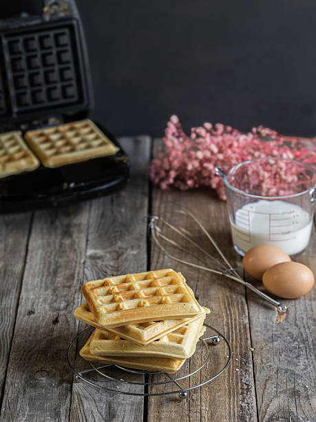 istock freshly made homemade waffles on a rack, ingredients on the side and waffle iron on the bottom. Rustic wooden table in a Nordic and intimate atmosphere. 2217458714