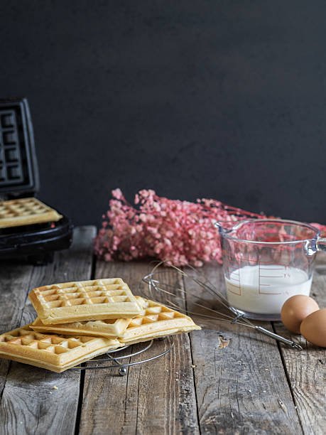 istock freshly made homemade waffles on a rack, ingredients on the side and waffle iron on the bottom. Rustic wooden table in a Nordic and intimate atmosphere. 2217458723