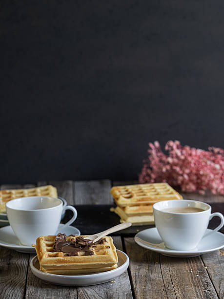 Rustic breakfast setup with coffee and waffles topped with chocolate spread, served on a wooden table in a cozy, home-style atmosphere.