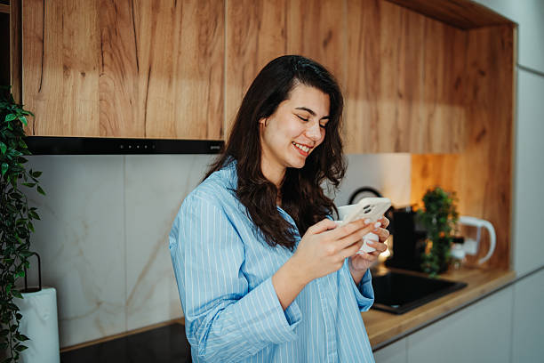 istock Young caucasian woman is using smartphone in the kitchen 2217462020
