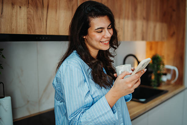 istock Young caucasian woman is using smartphone in the kitchen 2217462046