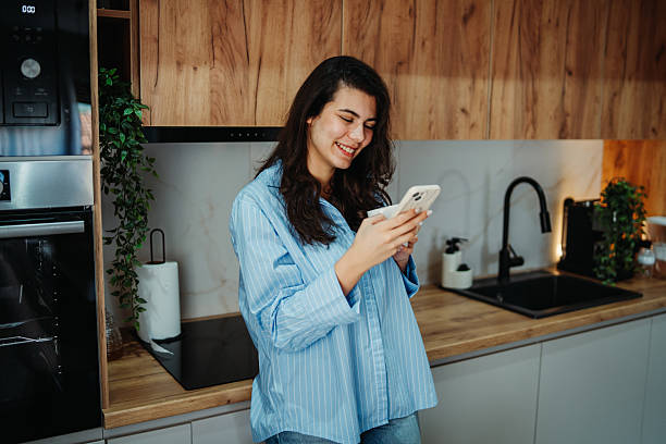 istock Young caucasian woman is using smartphone in the kitchen 2217462051