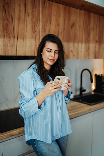 istock Young caucasian woman is using smartphone in the kitchen 2217462127
