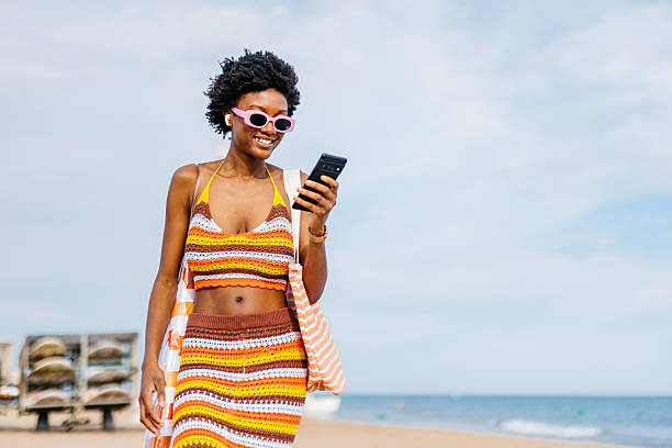 istock Young Black Woman Using Her Phone While Walking On The Beach In Spain 2217463587