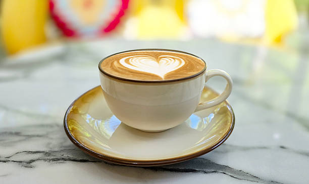 Heart shape latte art coffee in white cup on marble table with blur background