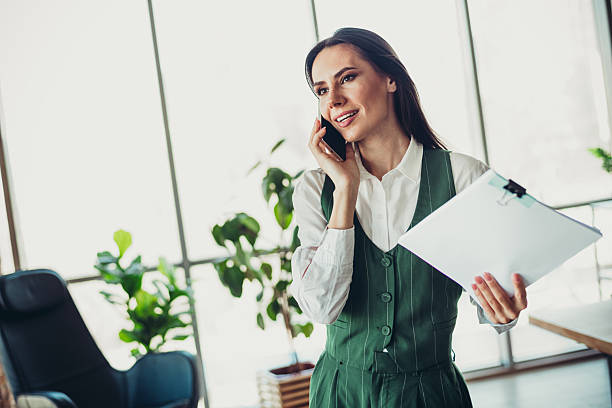 istock Confident businesswoman speaking on phone while holding clipboard in modern office environment 2217466853