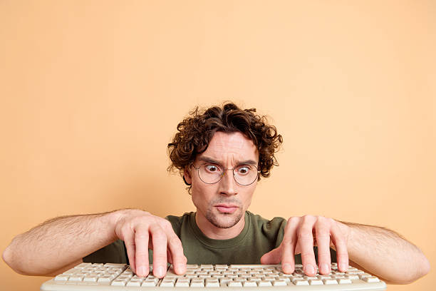 istock Young man wearing glasses typing on a keyboard with a focused expression against a beige background 2217467967