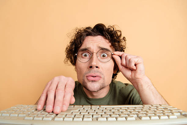istock Young curly haired man with glasses using a keyboard on a beige background for technology and lifestyle concepts 2217467968
