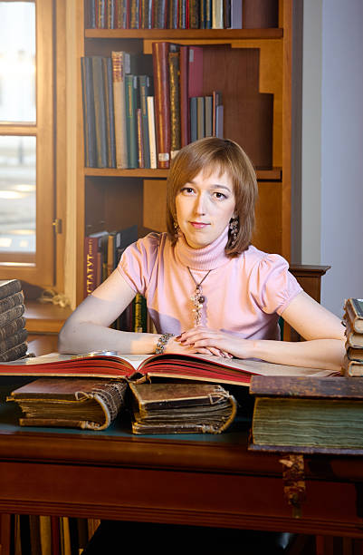 Cute young female student sitting at table with book, looking at camera