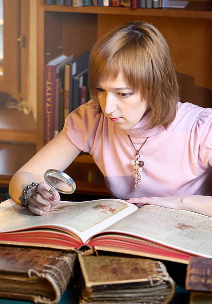 istock A cute young woman carefully examines an old tome using a magnifying glass while sitting at a table in a library 2217470470
