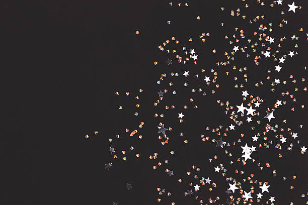 Silver colored stars and crystals confetti on a black background.