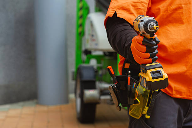 istock Close-up of a construction worker with a tool belt, wearing protective gloves, holding a cordless drill. Concept on a construction site with green industrial equipment. 2217479542