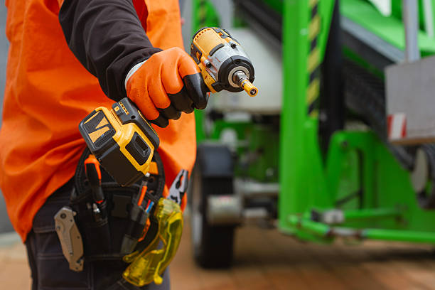 istock Close-up of a construction worker with a tool belt, wearing protective gloves, holding a cordless drill. Concept on a construction site with green industrial equipment. 2217479543