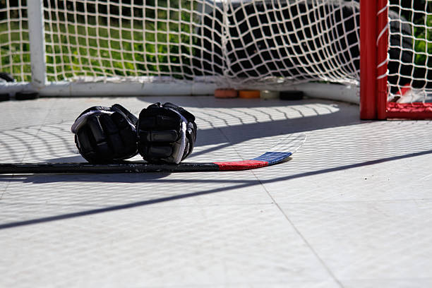 Ice hockey stick with gloves on shooting pad with net and pucks in the background