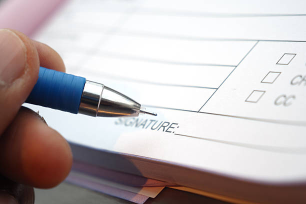 A hand is using a blue pen to sign a document with checkboxes.