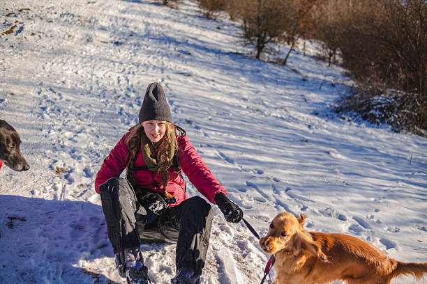 A woman wearing winter attire and her golden retriever enjoying a peaceful walk in a serene snowy forest during wintertime.