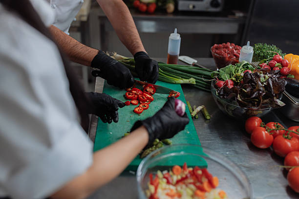 Chefs slicing red peppers and preparing other fresh vegetables in a commercial kitchen