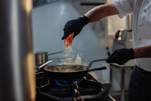 Professional chef adding a special sauce with a squeeze bottle to a hot pan in a restaurant kitchen