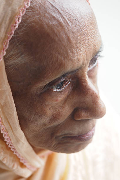 Happy elderly Asian woman lying in bed and peacefully looking out the window at home.