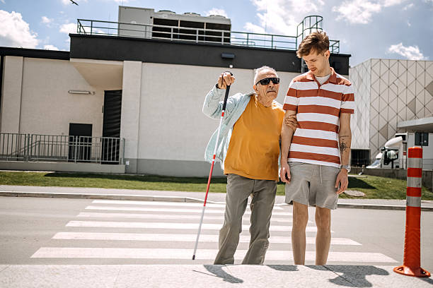 istock Young adult spending time with older blind man holding blind persons cane, outdoors walking over crosswalk 2217492175