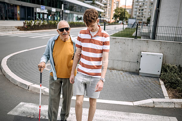istock Young adult spending time with older blind man holding blind persons cane, outdoors walking over crosswalk 2217492191