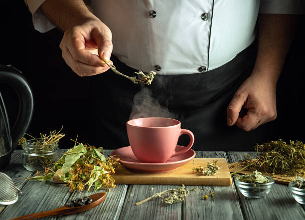 istock A chef adds fresh herbs to a steaming cup in a warm kitchen. The rustic wooden table holds various herbs, showcasing a blend of culinary tradition and creativity 2217493206